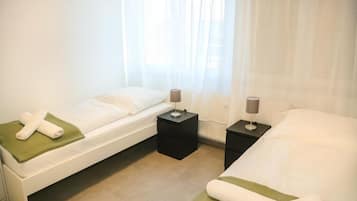 A hotel room with two beds, a window with sheer curtains, and bedside tables with lamps.