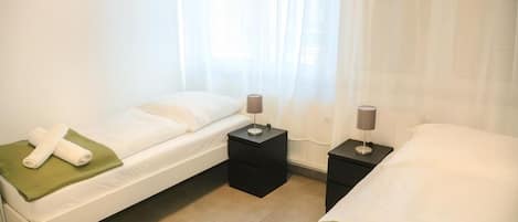 A hotel room with two beds, a window with sheer curtains, and bedside tables with lamps.