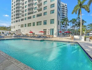 Ein Hotel mit Swimmingpool, Liegestühlen und roten Sonnenschirmen.