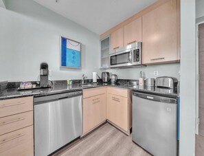 A modern kitchen with stainless steel appliances, wooden cabinets, and a countertop with various items. - Walk to Paradise - Bright & Cozy 2-Bedroom Fort Lauderdale Beach (Fort Lauderdale)