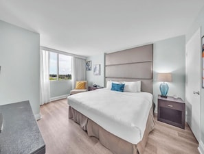 Ett hotellrum med en stor säng, ett skrivbord, en stol, ett nattduksbord och ett fönster med utsikt.