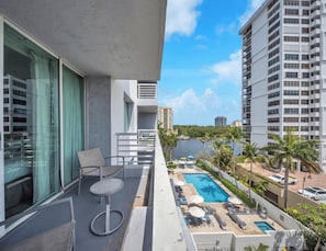 A balcony with a view of a swimming pool, lounge chairs, and a cityscape. - Walk to Paradise - Bright & Cozy 2-Bedroom Fort Lauderdale Beach (Fort Lauderdale)