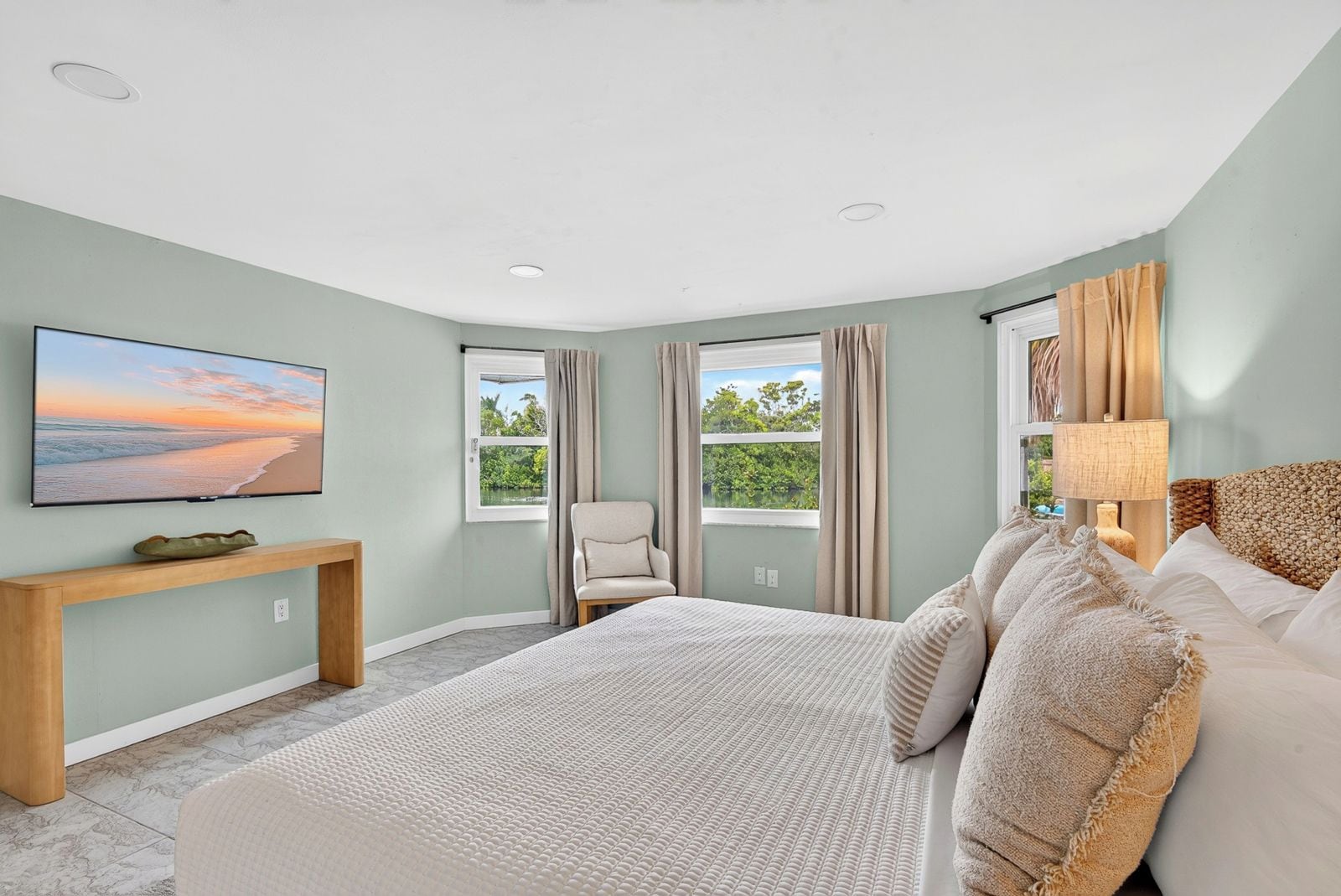 Ein Schlafzimmer mit einem Bett, einem Sessel, einem Fernseher und Fenstern mit Vorhängen.