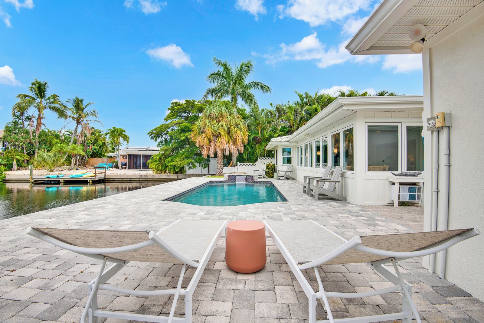 A poolside area with a rectangular pool, lounge chairs, and a small table.