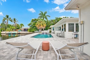 A poolside area with a rectangular pool, lounge chairs, and a small table. - Lakefront · Fishing · Heated Pool · Walk to Beach (Holmes Beach)