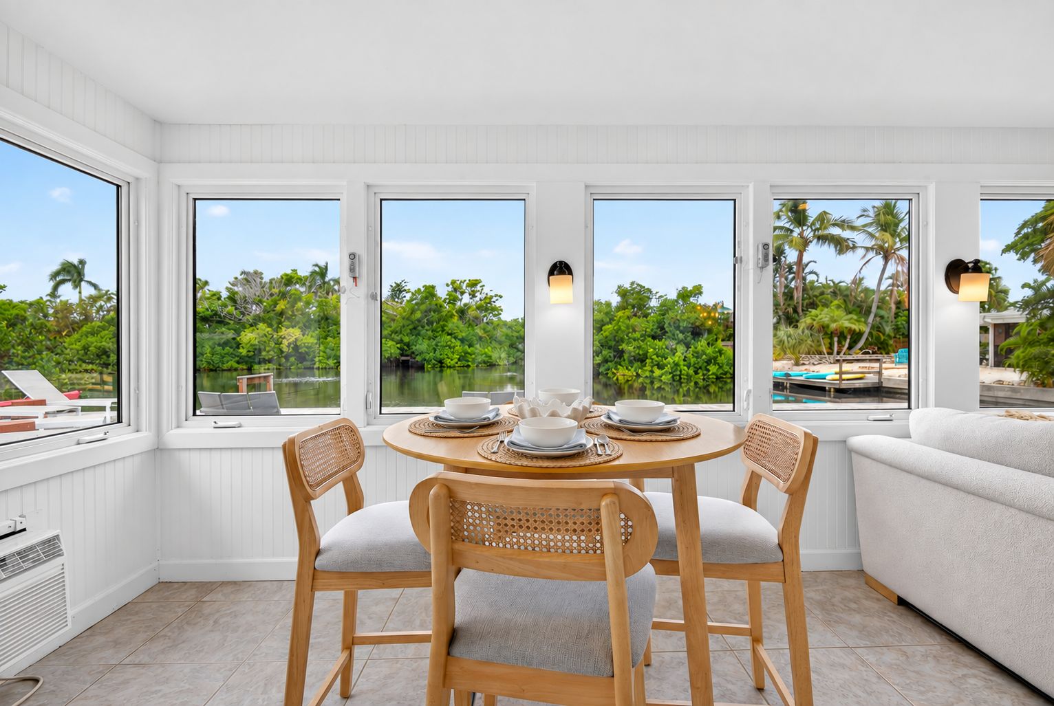 A dining area with a round table, four chairs, and a view of a pool and greenery.