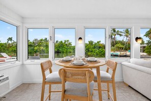 A dining area with a round table, four chairs, and a view of a pool and greenery. - Lakefront · Fishing · Heated Pool · Walk to Beach (Holmes Beach)