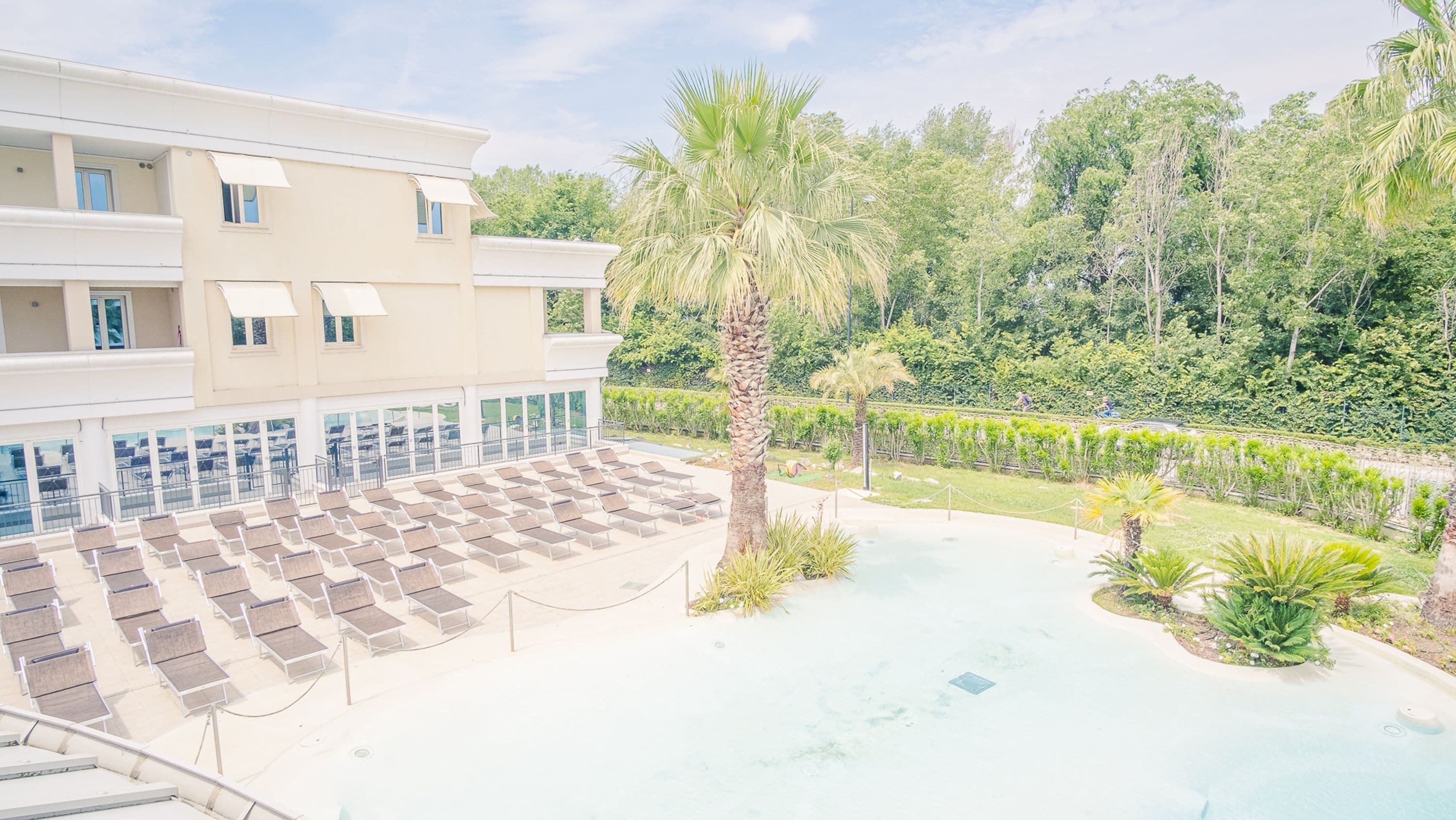 Un hôtel doté d’une piscine, de chaises longues et d’un palmier.