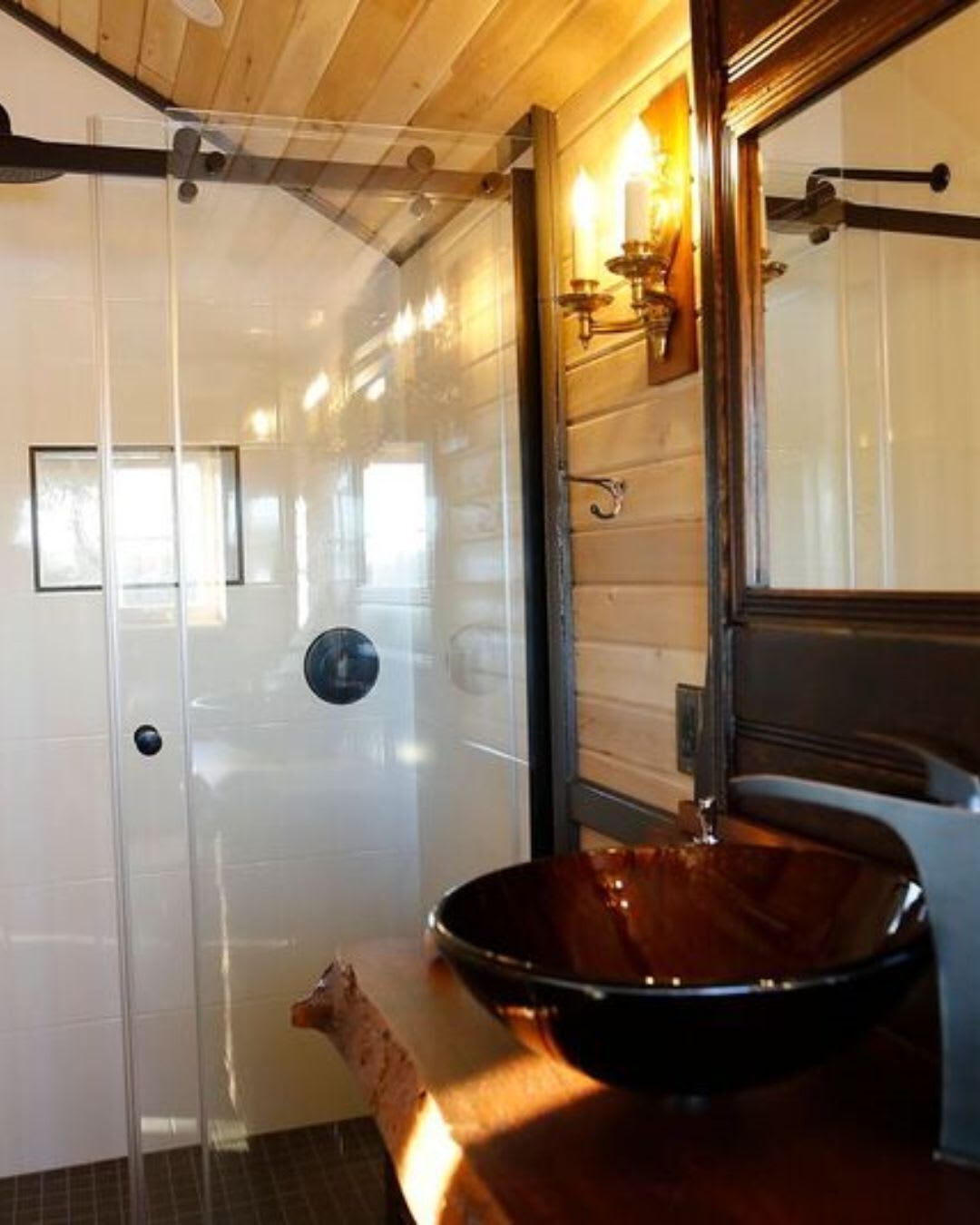 A bathroom with a glass shower enclosure, a wooden sink, and a mirror.
