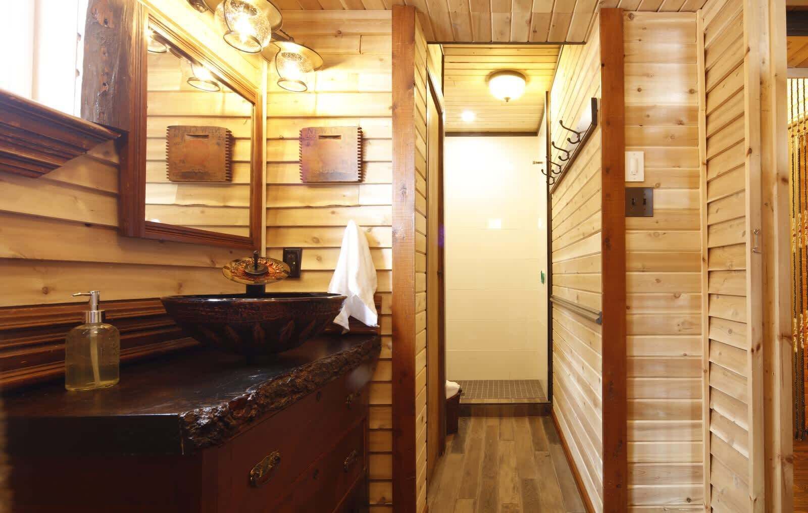 A narrow wooden bathroom with a wooden vanity, a mirror, and a light fixture above the mirror.