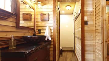 A narrow wooden bathroom with a wooden vanity, a mirror, and a light fixture above the mirror.