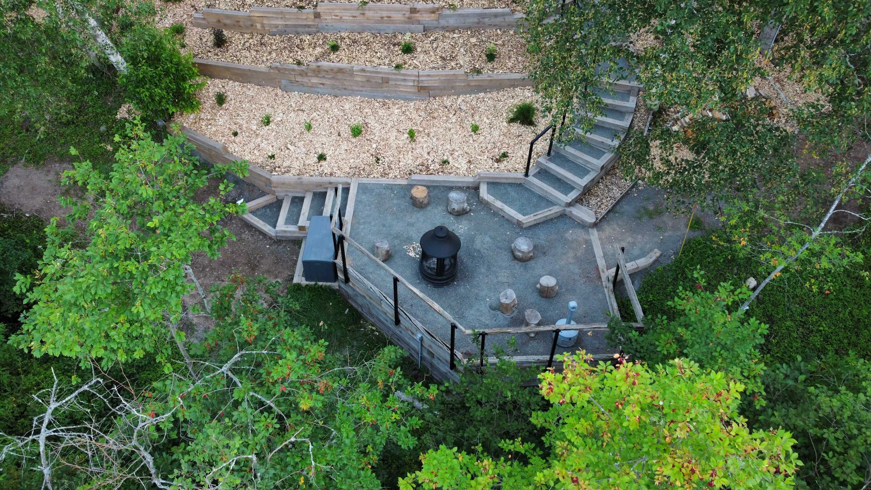 Un espacio de estar al aire libre con forma circular, que cuenta con una chimenea central, rodeado por un deck de madera y grava.