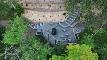 Un espacio de estar al aire libre con forma circular, que cuenta con una chimenea central, rodeado por un deck de madera y grava.