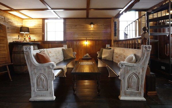 A room with a wooden floor, a central table, two white upholstered sofas, and a wooden wall with a window.