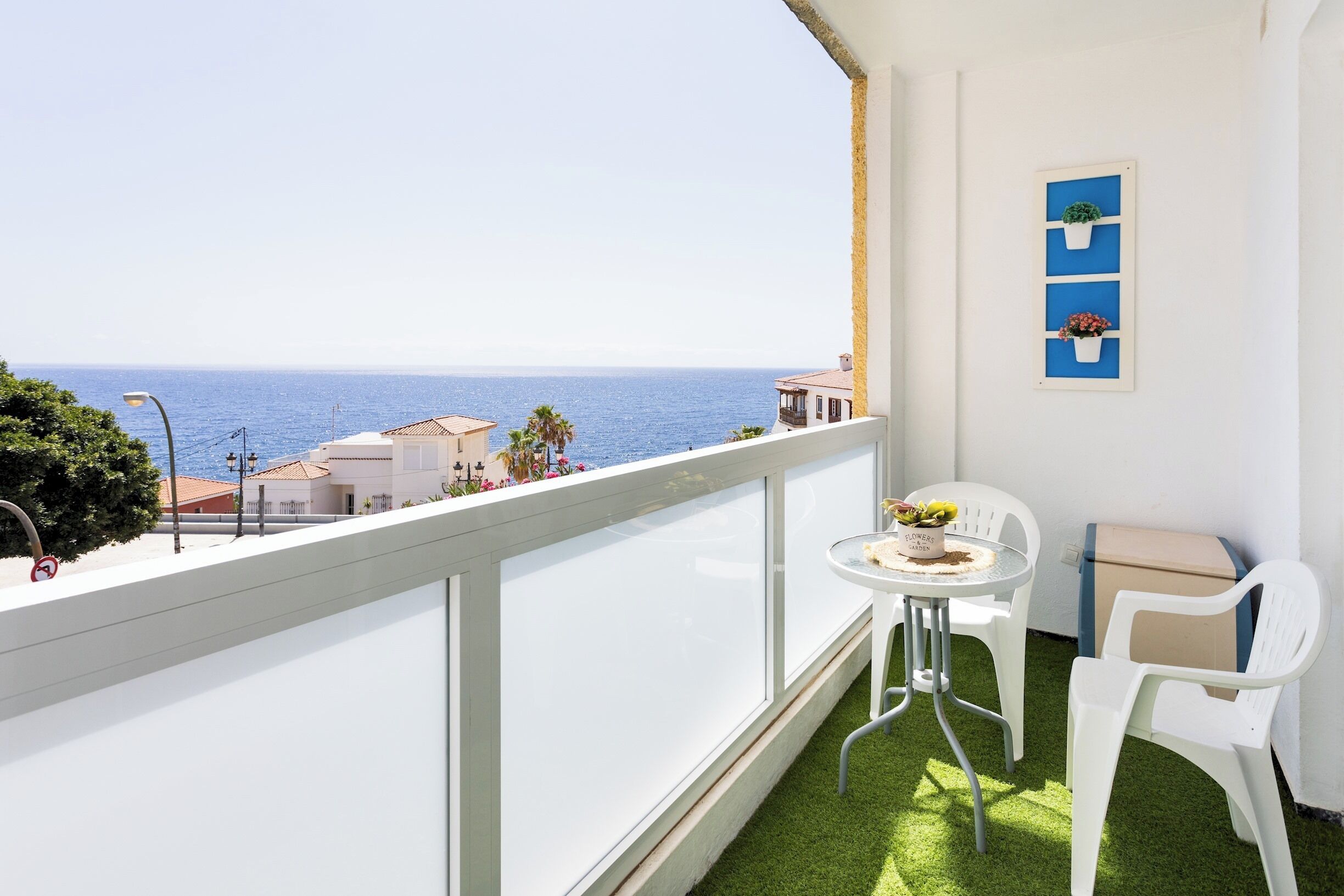 Un balcon avec vue sur la mer, une petite table avec un pot de fleurs et une chaise.