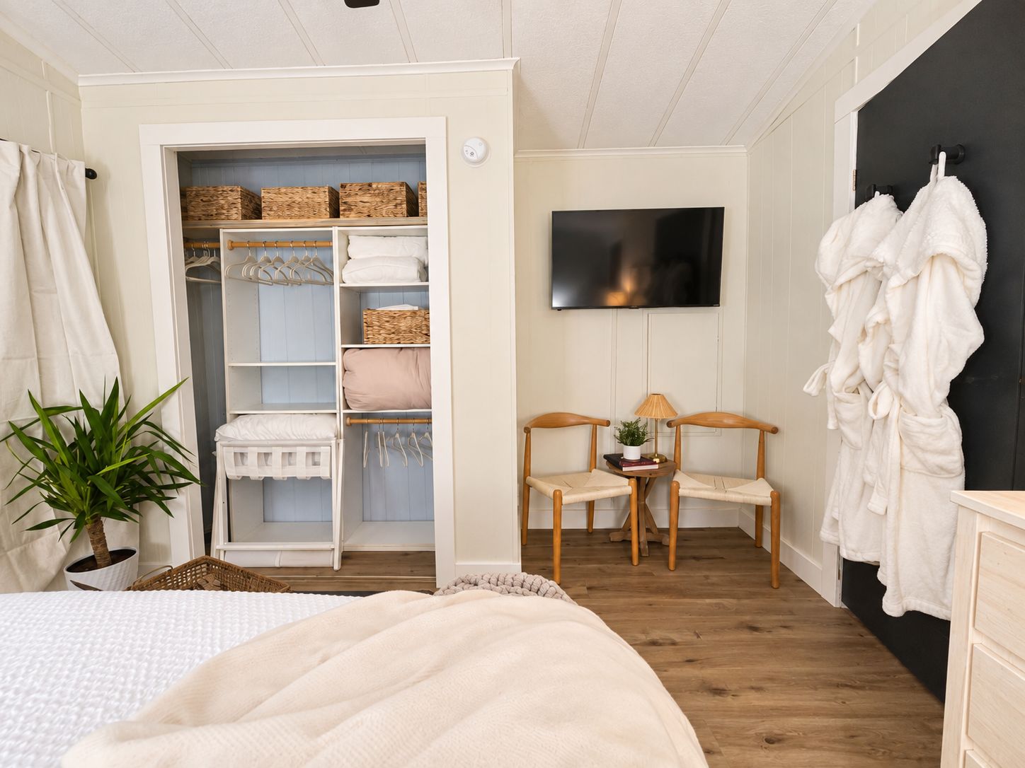 Une chambre à coucher avec un lit, une armoire, une télévision, deux chaises et une plante en pot.