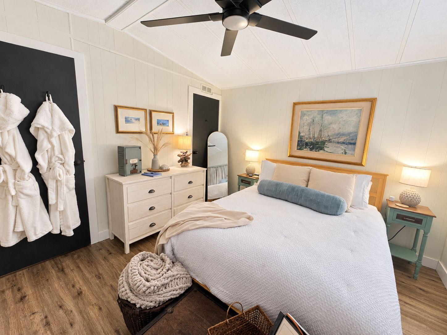 Un dormitorio con cama, cómoda, espejo, ventilador de techo y un cuadro en la pared.