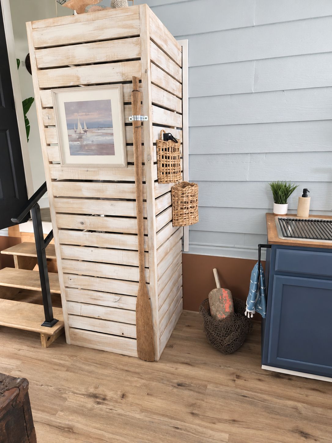 Un mueble de almacenamiento de madera con un marco de fotos, cestas y una escoba.