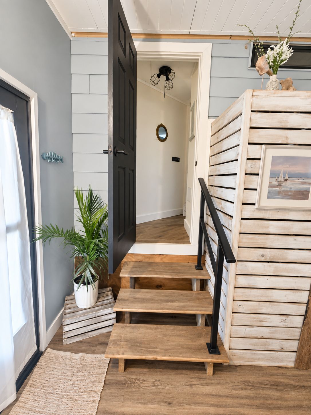 Una escalera con escalones de madera y barandilla negra, que lleva a una habitación con ventilador de techo y un pequeño espejo en la pared.