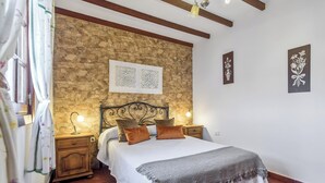 Een slaapkamer met een stenen muur, een bed met een witte spreideken, twee bedlampen en een nachtkastje.
