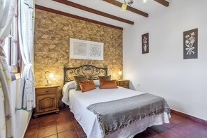 Ein Schlafzimmer mit Steinwand, einem Bett mit weißer Bettdecke, zwei Nachttischlampen und einem Nachttisch.