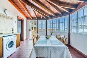 Un coin repas avec une table dressée pour quatre personnes, des poutres en bois au plafond et de grandes fenêtres.
