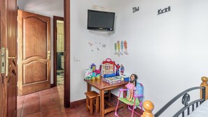 Een kinderspeelkamer met een houten deur, een aan de muur bevestigde televisie en diverse speelgoedjes en decoraties.