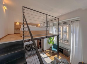 Ein modernes Interieur mit einer Holztreppe, einem Bett, einem Schreibtisch und Blick ins Freie.