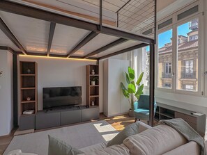 Ein modernes Wohnzimmer mit Flachbildfernseher, Einbauschränken, einem großen Fenster und einer gemütlichen Sitzecke.