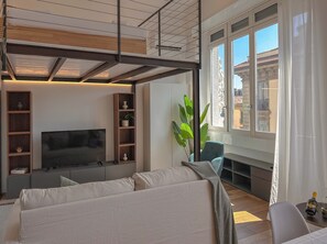 Un salon moderne doté d’un téléviseur à écran plat, d’étagères intégrées, d’un canapé, d’une grande fenêtre avec des rideaux et d’une plante en pot.