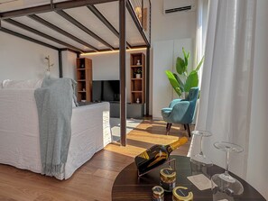 Ein modernes Wohnzimmer mit einer Couch, einem Couchtisch mit einer Flasche und Weingläsern, einem Bücherregal und einer großen Pflanze.