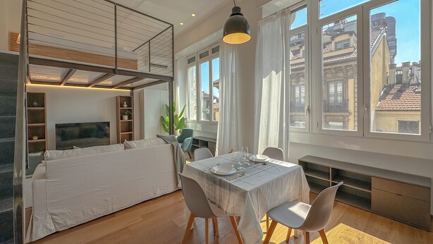 Ein moderner Essbereich mit einem Tisch für zwei Personen, einer Couch und Blick auf die Stadt durch große Fenster.
