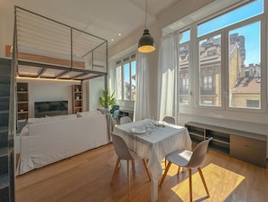 Un'elegante sala da pranzo con un tavolo apparecchiato per due persone, un divano e vista sulla città attraverso ampie finestre.