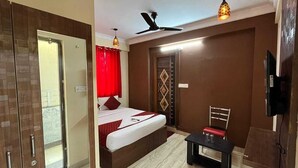 A bedroom with a bed, a desk, a chair, a television, and a ceiling fan. - Tanish Stay Inn (Bengaluru)