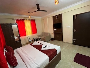 Ein Hotelzimmer mit einem Bett, einem Sessel, einem Schreibtisch, einem Fernseher und einem Kleiderschrank.