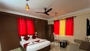 A hotel room with a bed, a chair, a small table, and a television. - Tanish Stay Inn (Bengaluru)