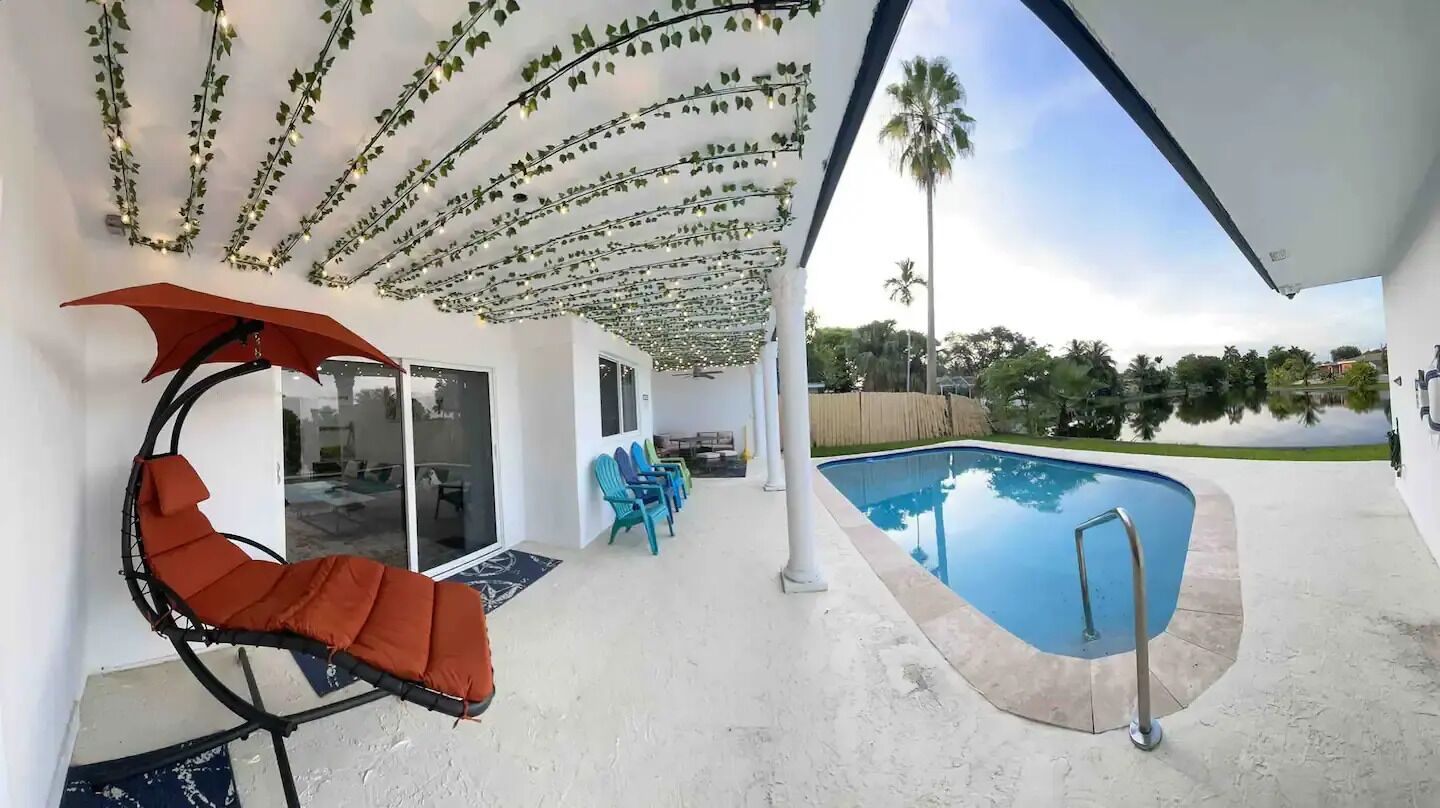 A covered outdoor area with a pool, a red chair, and a row of blue chairs.