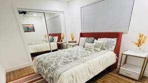 A bedroom with a large bed, a ceiling fan, a window with blinds, a mirror, and a small bedside table with a vase of flowers. - Lakefront home with private pool near Miami (Miramar)
