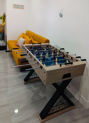 Ein Tischkicker in einem Raum mit einem gelben Sofa und einer Wandpflanze.