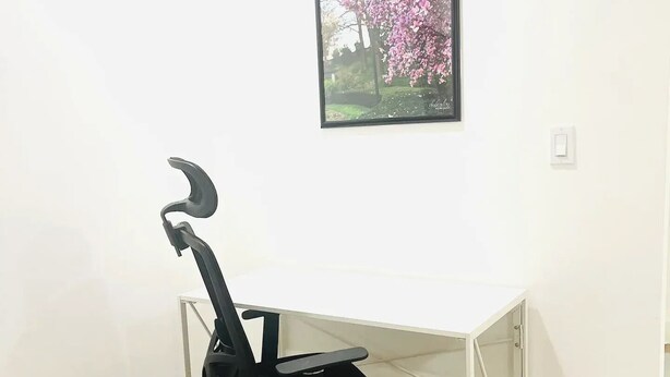 A room with a white wall, a wooden floor, a black office chair, and a framed picture of pink flowers on the wall. - Lakefront home with private pool near Miami (Miramar)
