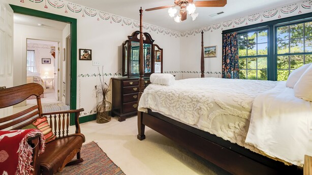 A bedroom with a four-poster bed, a wooden chair, a dresser, and a mirror.