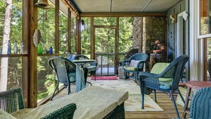 A covered outdoor seating area with wicker furniture, a stone wall, and a view of the forest.