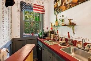 Una cocina con ventana, un lavamanos y diversas botellas y vasos sobre la encimera.