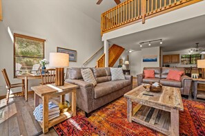Ein geräumiges Wohnzimmer mit hoher Decke, einer Treppe und einem Essbereich mit Holzmöbeln.