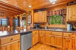 A wooden cabin interior with a kitchen area featuring wooden cabinets, a dishwasher, and a window with a view of greenery. - Incredible MTN Views*Hot Tub + Game Room*Fireplace (Pigeon Forge)