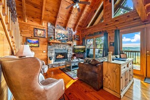 A log cabin interior with a fireplace, leather furniture, and a scenic view through the windows. - Incredible MTN Views*Hot Tub + Game Room*Fireplace (Pigeon Forge)