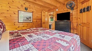 A wooden cabin room with a bed, a dresser, a television, and a bear decoration on the wall. - Incredible MTN Views*Hot Tub + Game Room*Fireplace (Pigeon Forge)