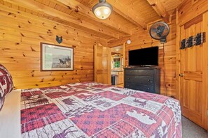 A wooden cabin room with a bed, a dresser, a television, and a bear decoration on the wall. - Incredible MTN Views*Hot Tub + Game Room*Fireplace (Pigeon Forge)