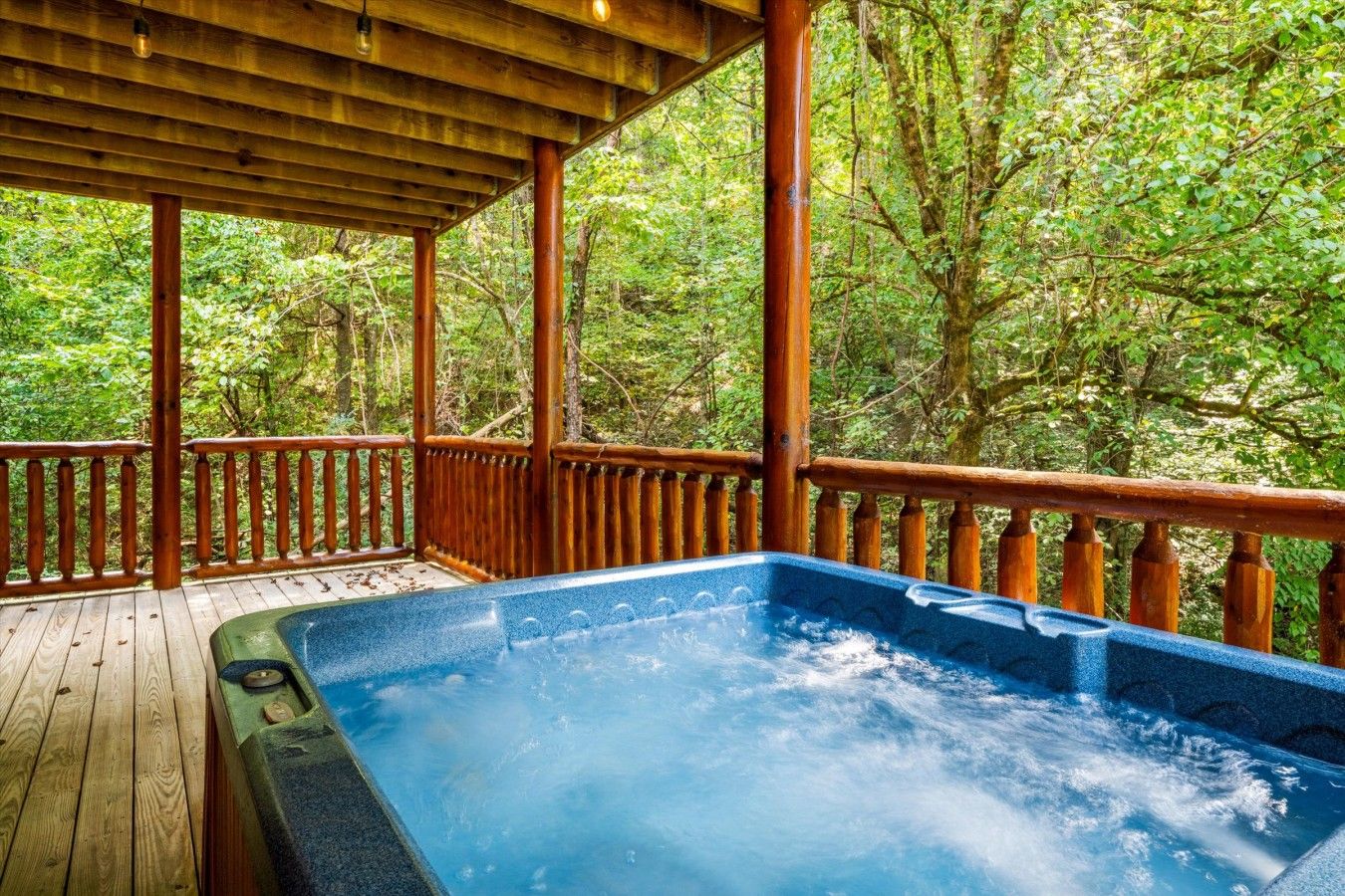 A hot tub under a wooden deck with a view of a forested area.