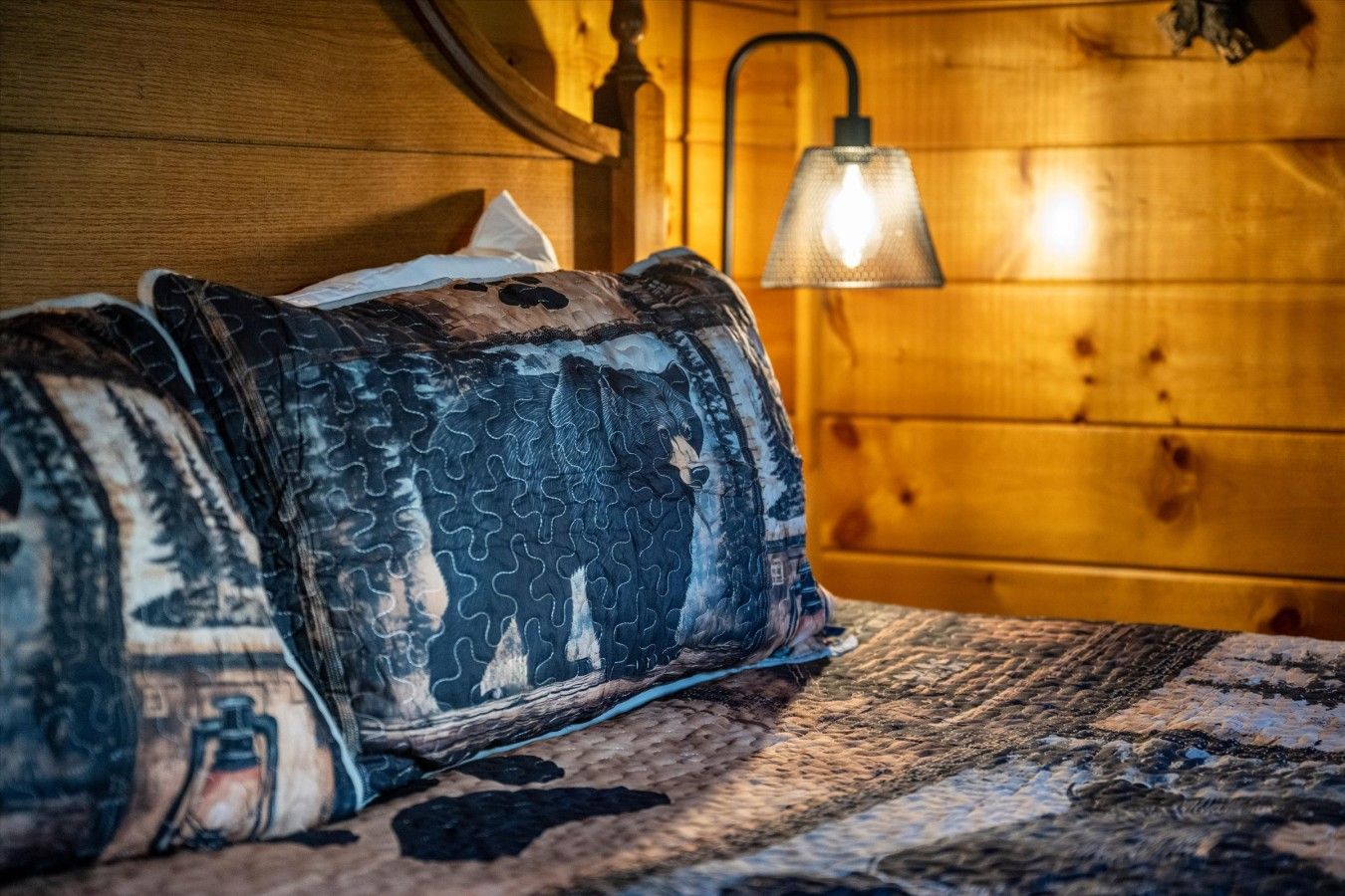 Un lit recouvert d’une courtepointe à motifs et une lampe dans une pièce en bois.